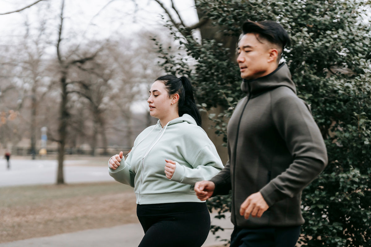 Plus sized female running with Asian trainer in park